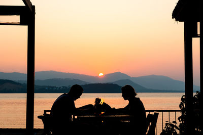 Silhouette people sitting by lake against sky during sunset