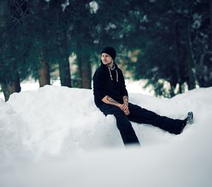 Thoughtful man sitting on snow covered field against trees