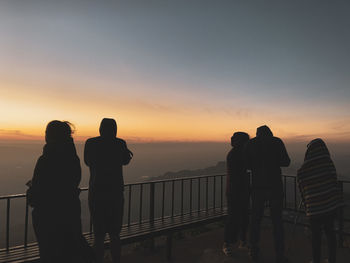 Silhouette people on railing against sky during sunset