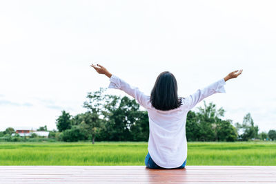 Rear view of woman with arms raised against sky