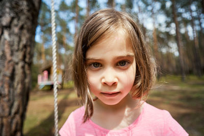 Adorable little girl sits on a swing and makes faces in the summer forest
