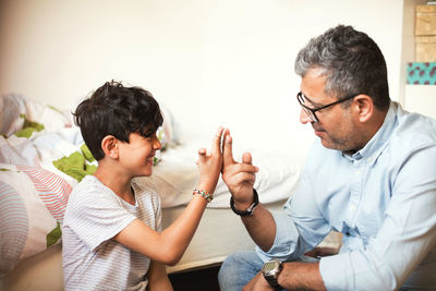 Smiling father and son playing with rubber bands while sitting at home