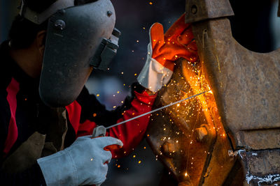 Welder in iron mask helmet welds with electric arc steel welding, industrial worker at the factory