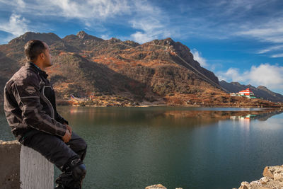 Man sitting by lake against sky