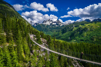 Man photographing while standing on sky pilot suspension bridge against sky