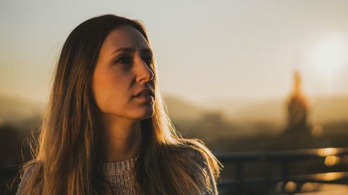 Portrait of beautiful young woman standing against sky during sunset