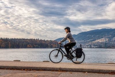 Side view of man riding bicycle by lake against sky