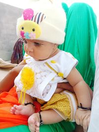 Cute baby girl looking away while sitting on woman at home