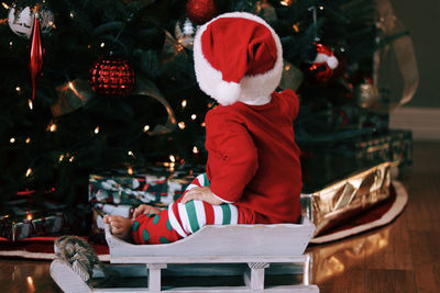 Boy sitting against christmas tree