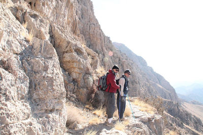 Rear view of men on rock in mountains against sky