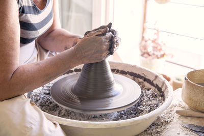 Midsection of woman making pot with clay on pottery wheel