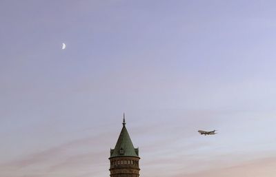 Minimalist view of tower against sky with moon and airplane