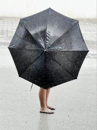 Woman holding umbrella while standing at beach in rainy season