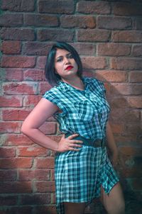 Portrait of young woman standing against brick wall