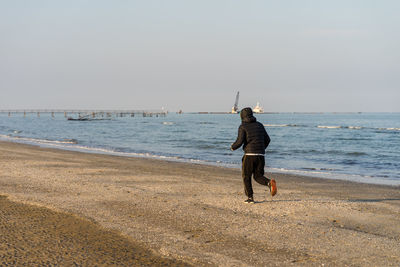 Rear view of man standing on beach against sky