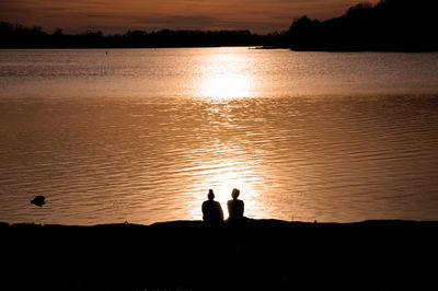 Silhouette friends on shore against sky during sunset