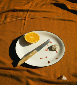 Plate with half an orange and knife on an orange scarf