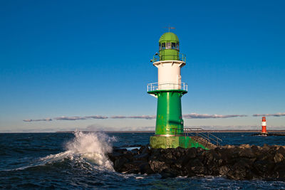 Lighthouse by sea against clear blue sky