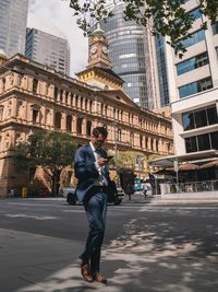 Full length of man holding umbrella on road against buildings in city