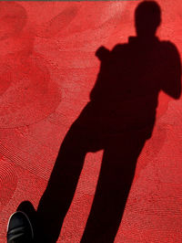 Low section of person standing by red shadow on wall