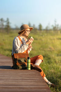 Naturalist woman resting on boardwalk, drinking tea, enjoying the moment at sunset. ecotourism