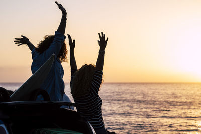 Happy female friends at beach against clear sky during sunset