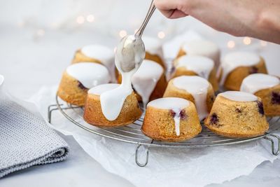 Close-up of hand holding cream on sweet food at cooling rack