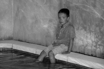 Portrait of cute boy sitting by swimming pool 