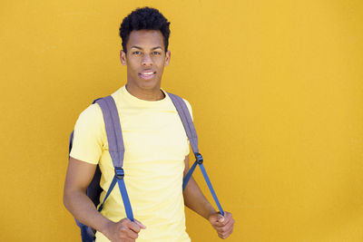 Portrait of young man standing against yellow background