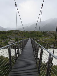 Footbridge leading towards mountains against sky