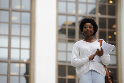 Woman holding papers while standing outdoors