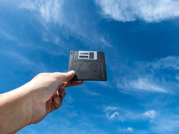 Hand holding a floppy a disc, insert the reader. technology  shape the background is the sky