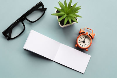 Notepad with reading glasses, pen and alarm clock on blue background. directly above. flat lay.