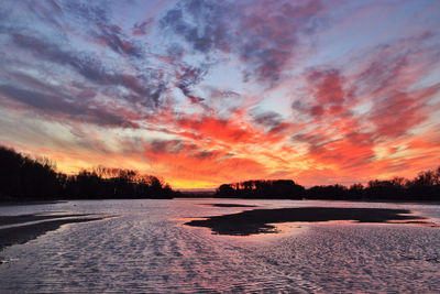 Scenic view of lake against dramatic sky during sunset