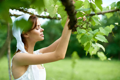 Side view of young woman standing by plants