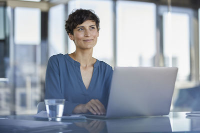 Smiling businesswoman sitting at desk in office with laptop
