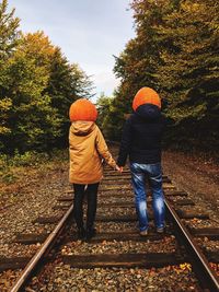 Rear view of couple with pumpkin head standing at railroad track during autumn