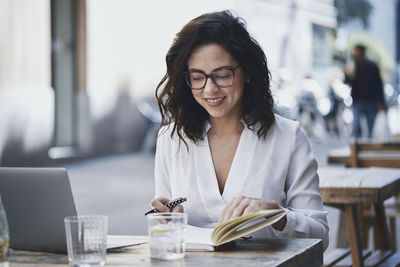 Smiling businesswoman writing in diary while sitting at sidewalk cafe