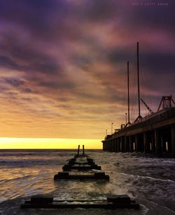 Pier on sea against cloudy sky at sunset