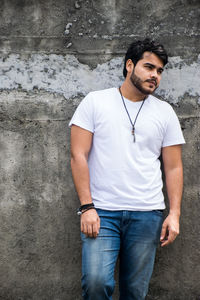 Young man looking away while standing against wall