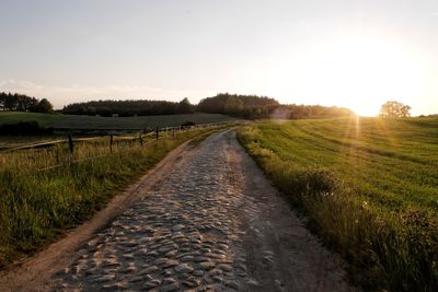 Dirt road amidst field against sky