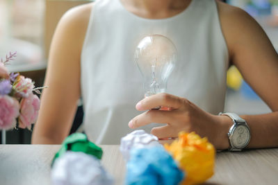 Midsection of woman holding light bulb by crumpled paper balls on table