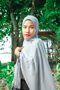 Portrait of young woman standing against trees