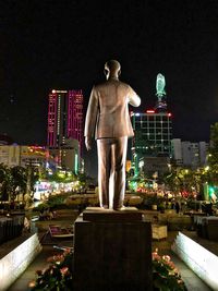 Statue against illuminated buildings in city at night