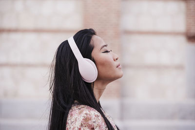 Woman with eyes closed wearing headphones outdoors