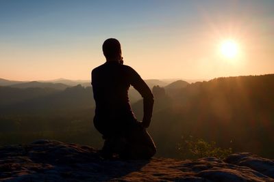 Sportsmann hiker in black sportswear sit on mountain top and take a rest with watching down