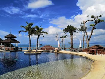 Palm trees by swimming pool by sea against sky