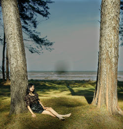 Side view of woman on tree trunk against sky