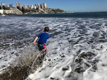 Rear view of boy playing at beach against sky