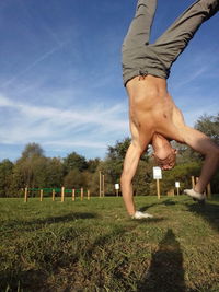 Shirtless man practicing handstand at park against blue sky